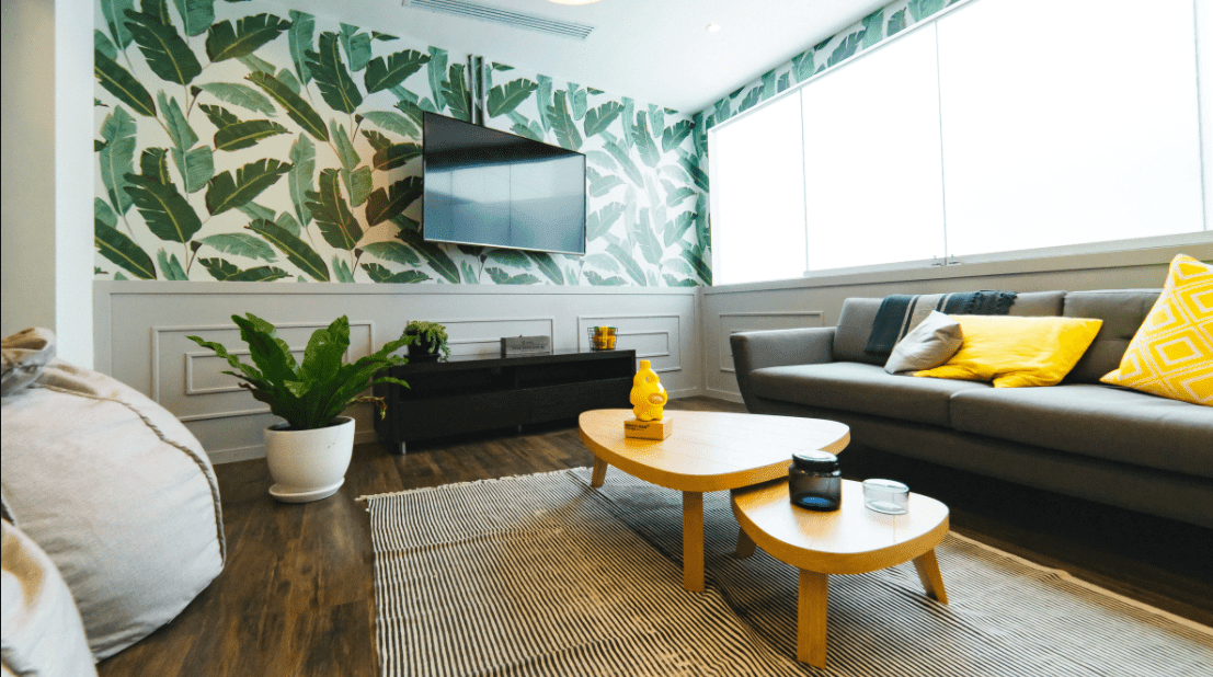 A cozy living room with a tiered coffee table, bean bags, and tropical wallpaper