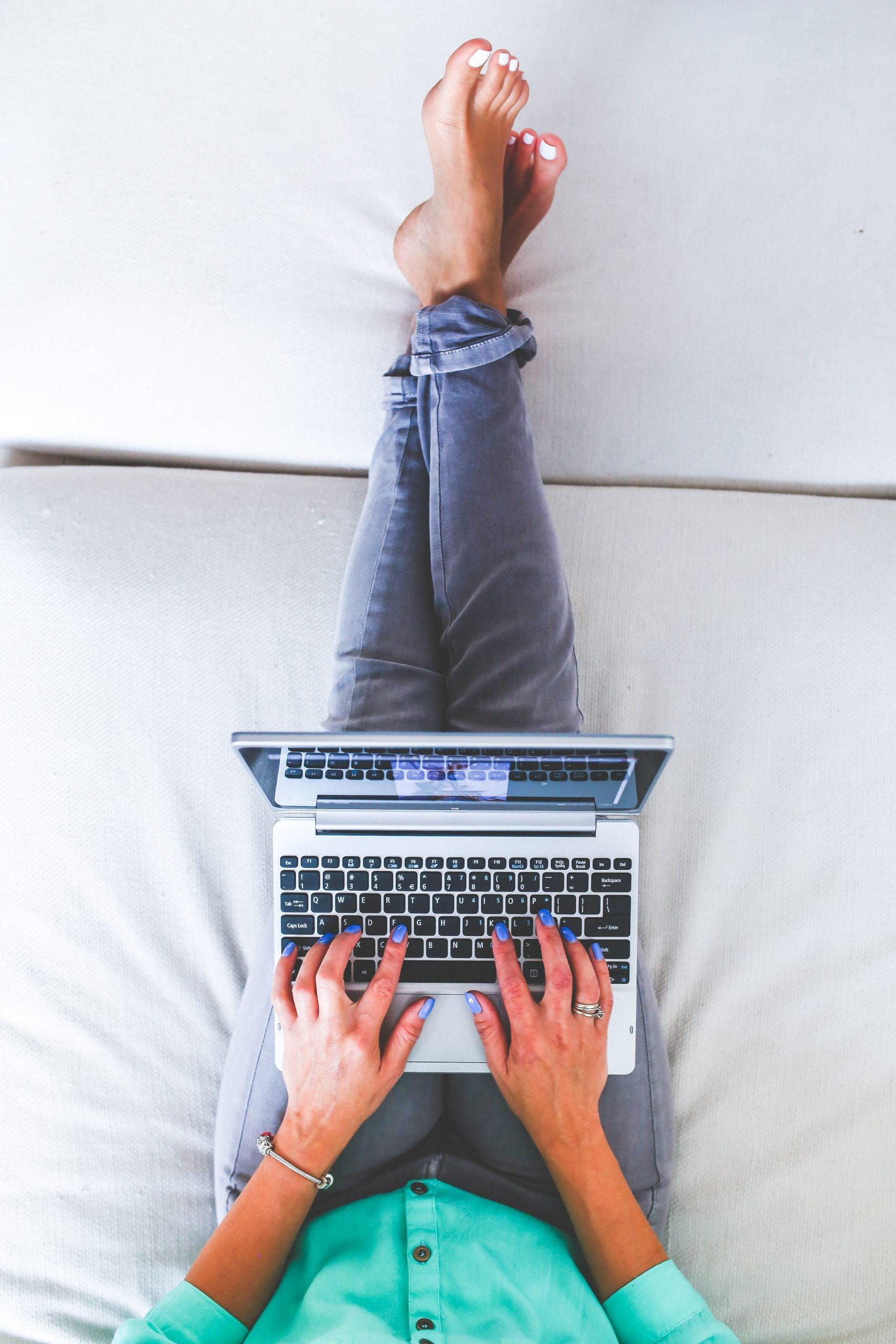 woman lying and typing on laptop, engaged in remote work