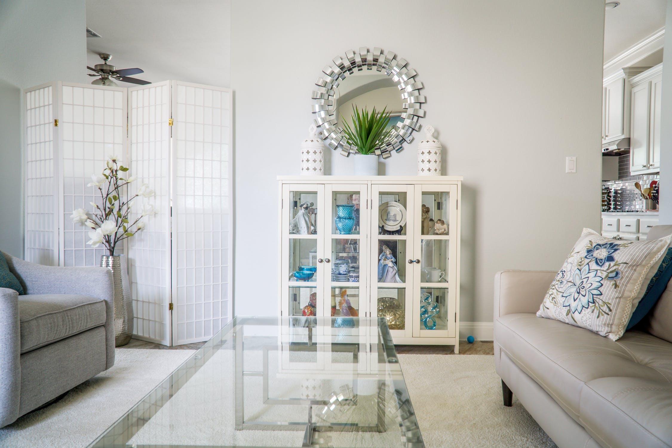 n all-white living room with a glass coffee table and a vintage white cabinet.